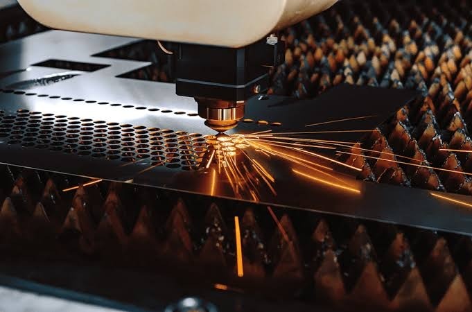 Cabezal láser CNC cortando una chapa de acero con chispas saltando sobre la mesa de corte