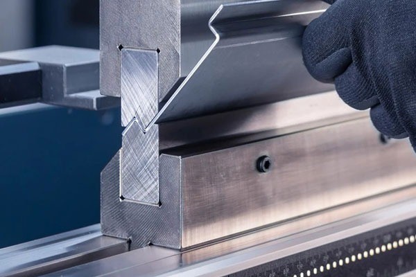Plegadora CNC doblando una pieza de chapa metálica con la mano del operario guiándola